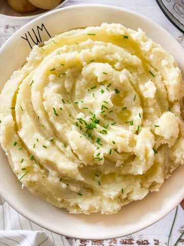 Hand holding up plate of mashed potatoes.