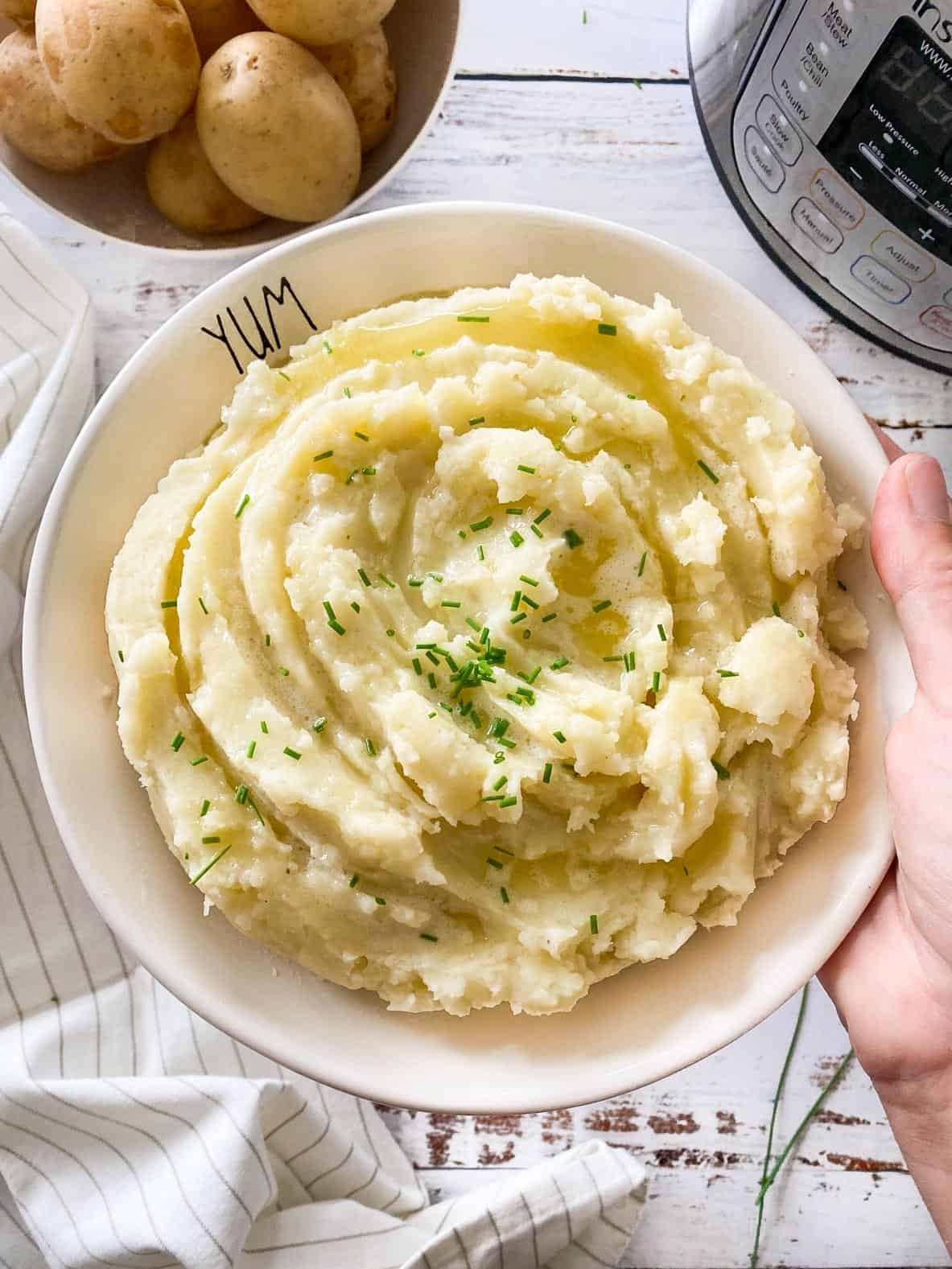 Hand holding up large plate of mashed potatoes with chives garnished on top.