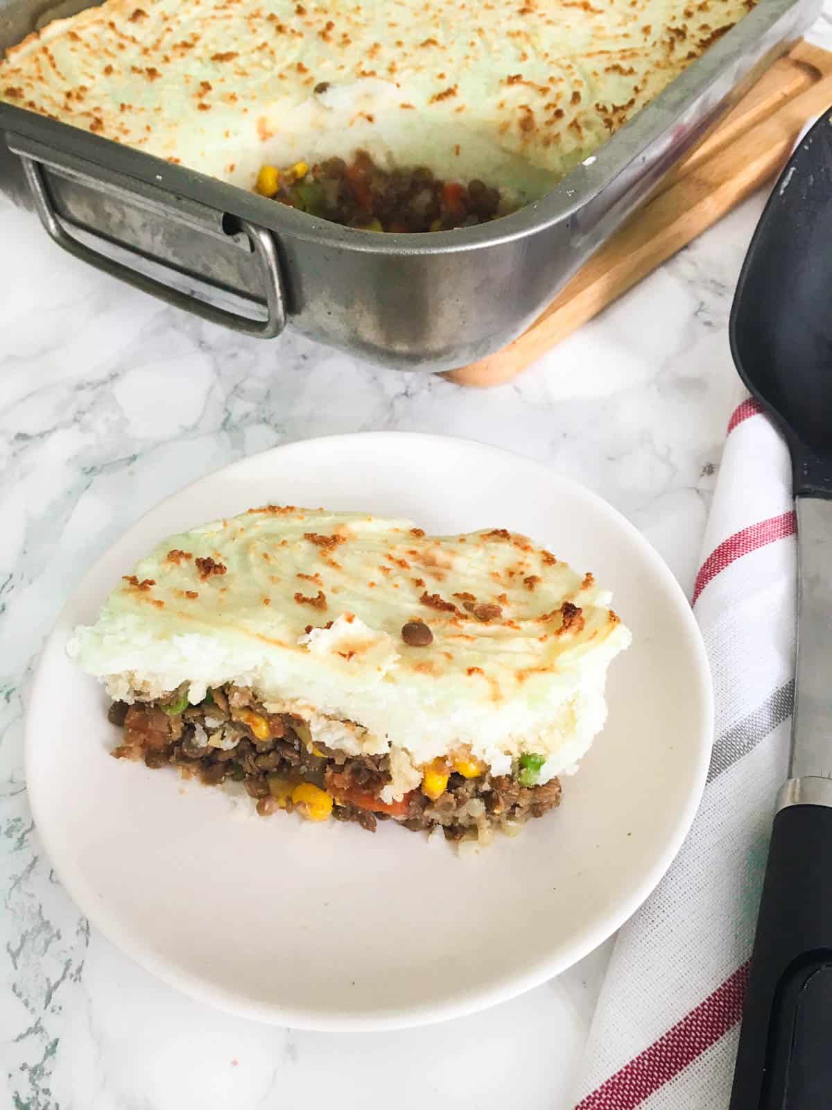 Lentil shepherd's pie on small white dish with tray in the background.