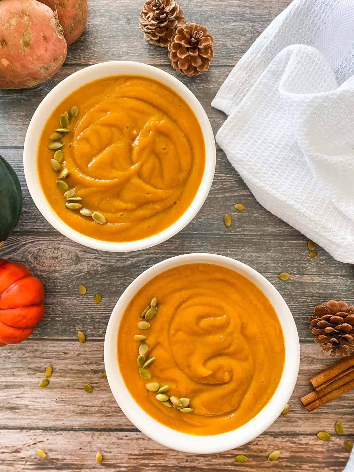 two bowls of pumpkin soup with pumpkin seeds garnished on top and white towel in background.