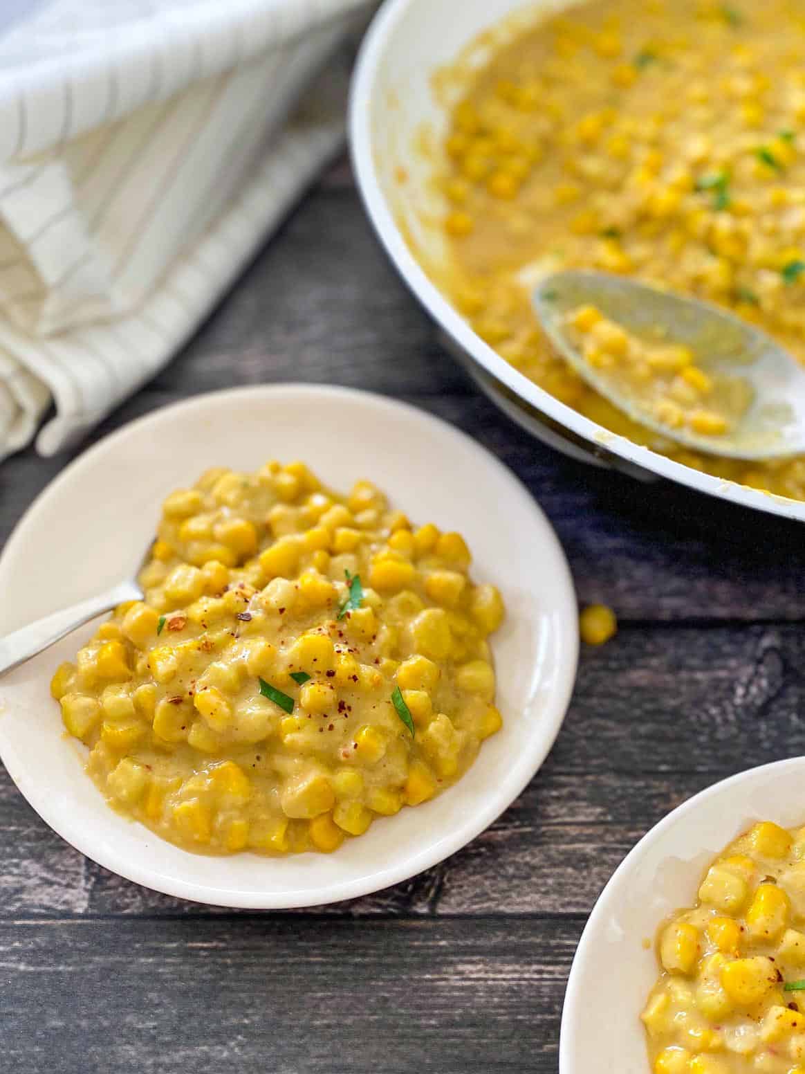 Creamed corn in white dish with spoon on the side and parsley garnish.