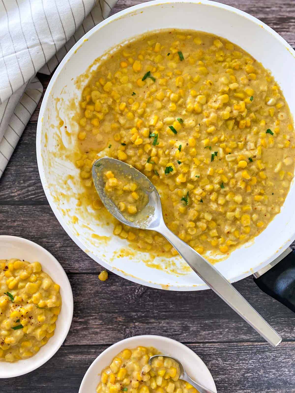 Skillet filled with creamed corn with large spoon resting inside.
