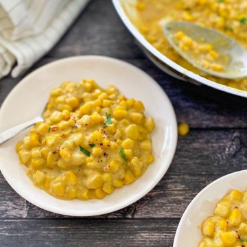 creamed corn in small white dish with spoon with pan of it in background.