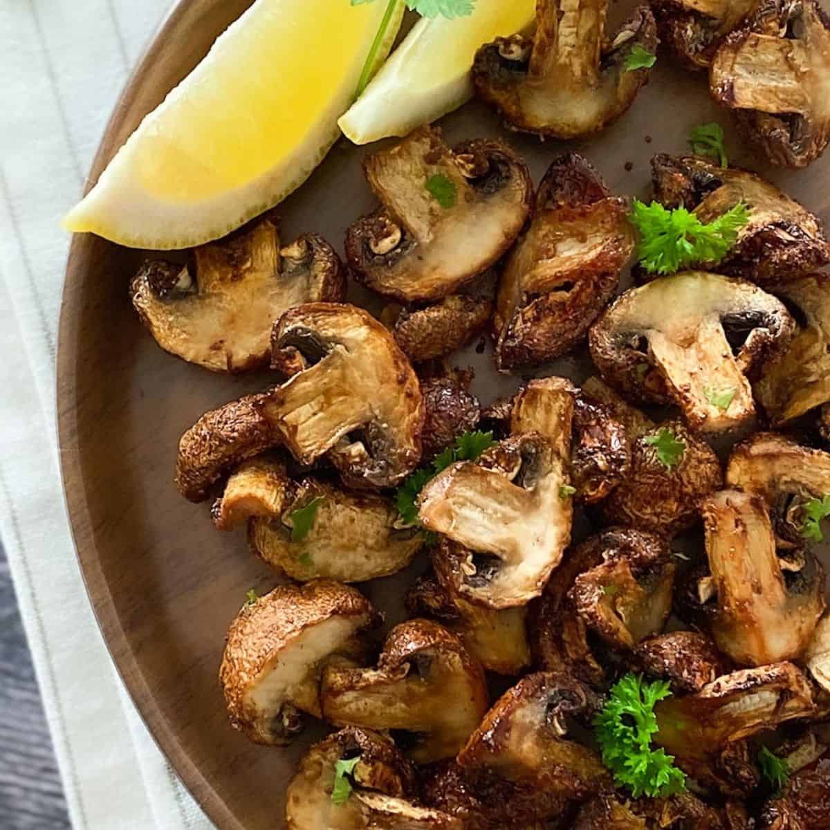 air fried mushrooms on brown plate with lemon wedges on the side.