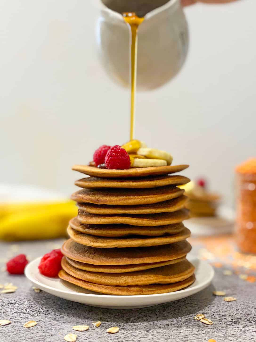 Pouring syrup over stack of pancakes with fruit on top of stack.