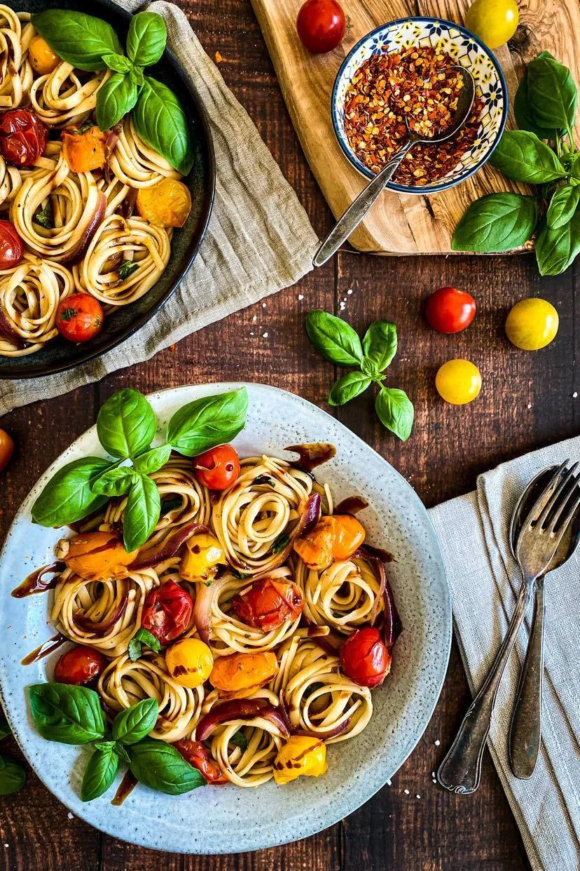 Plate of twirled linguini with cherry tomatoes and basil on top.