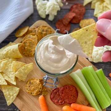vegan walnut cheese sauce in glass container with hand holding dipped chip above it.