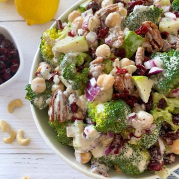 Large salad in white serving bowl with lemons, pecans, and cranberries around it.