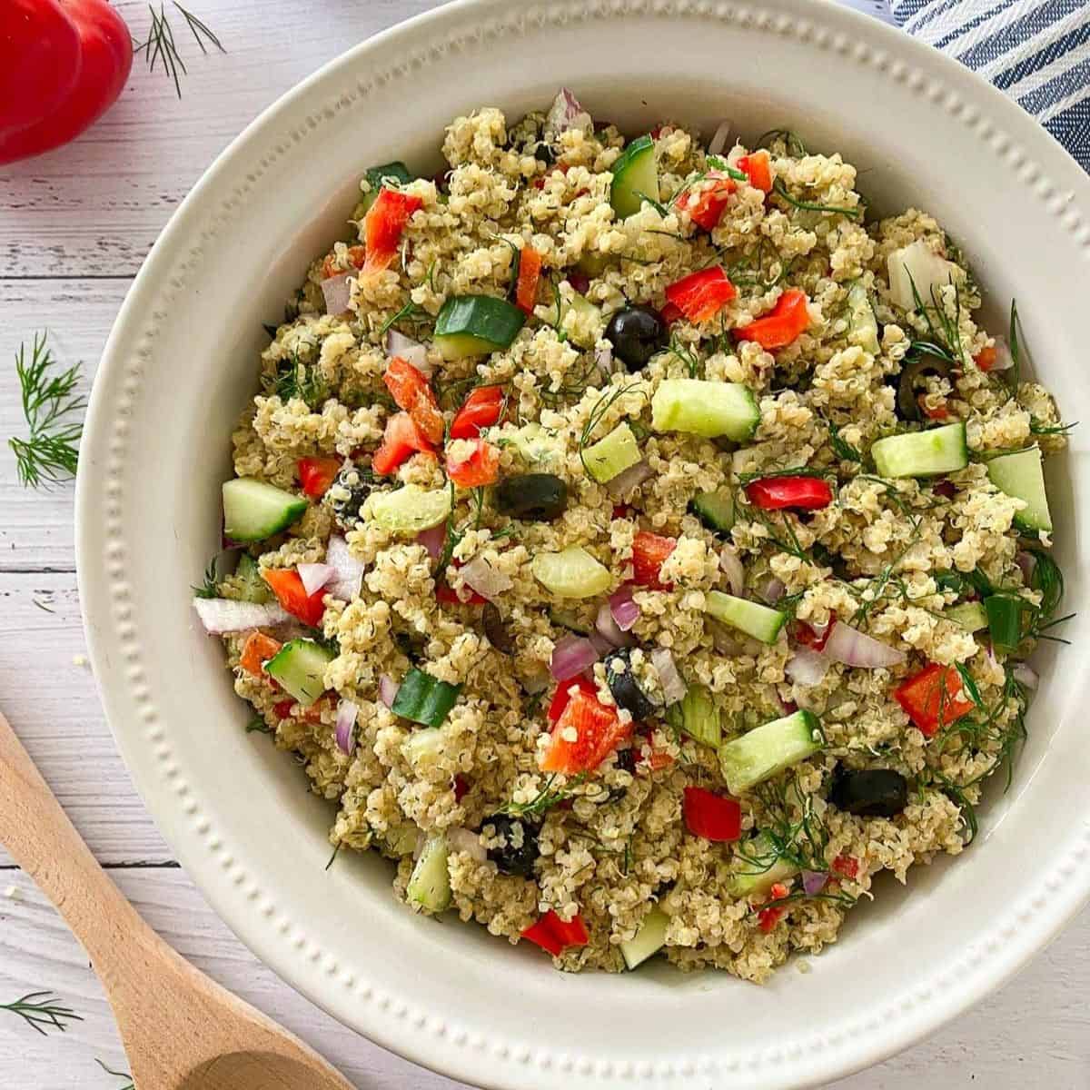 Large bowl of quinoa salad with red pepper, olives, and cucumber.