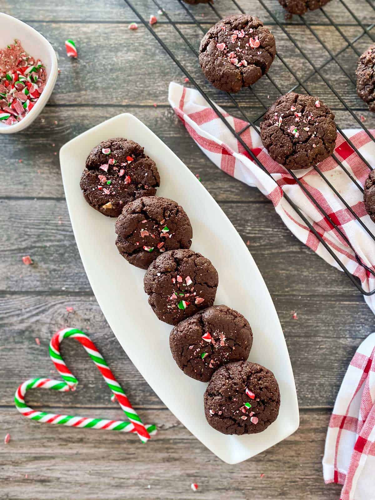 Chocolate cookies with candy cane pieces on top in a white serving dish.