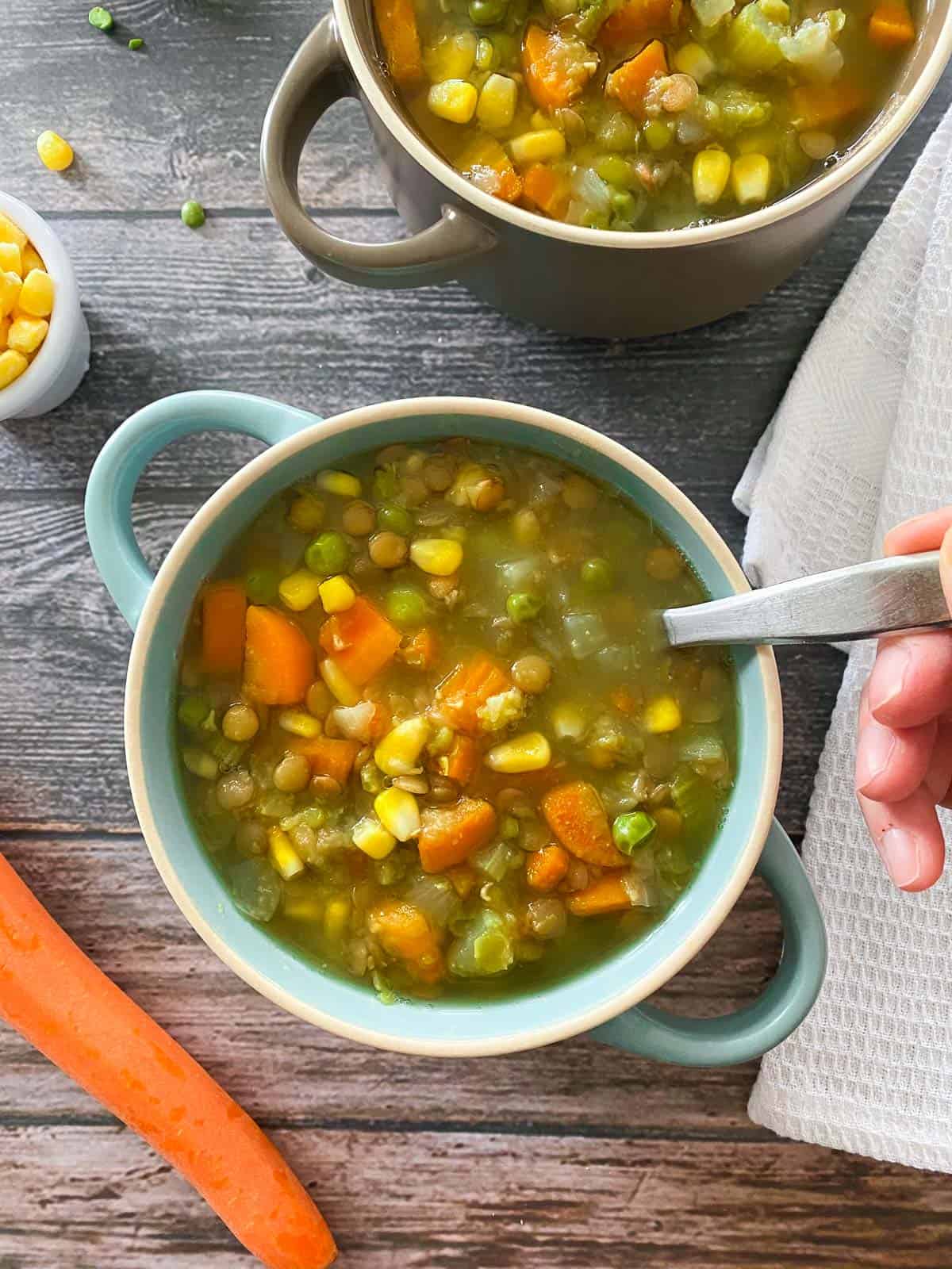 Hand holding spoon inside bowl of lentil split pea soup.