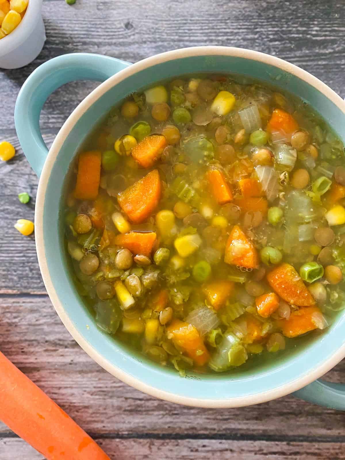 Blue bowl of soup with lentils, peas, carrots, onion, celery and broth.