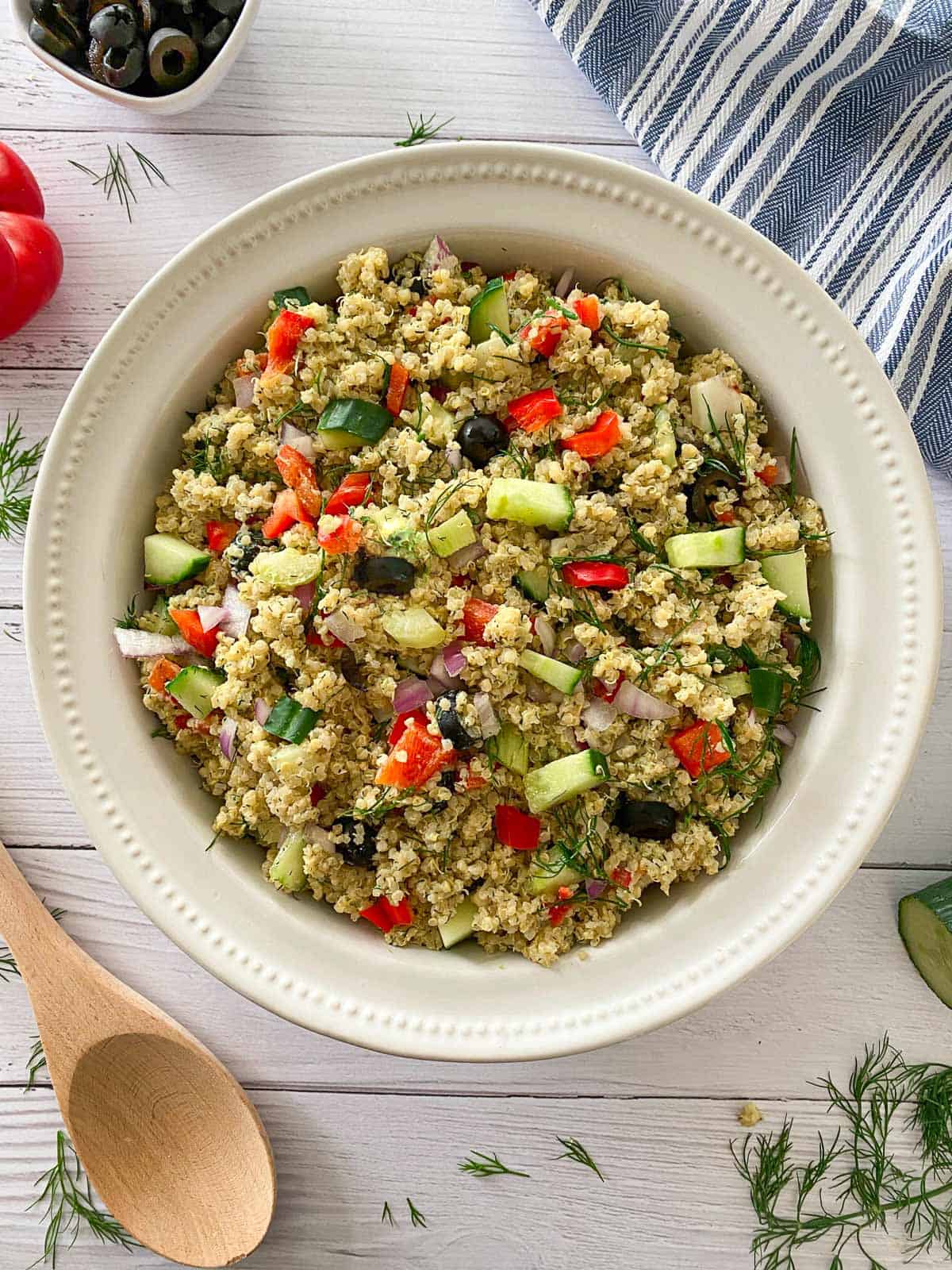 Large white bowl with quinoa, cucumber, red pepper, olives and dill.