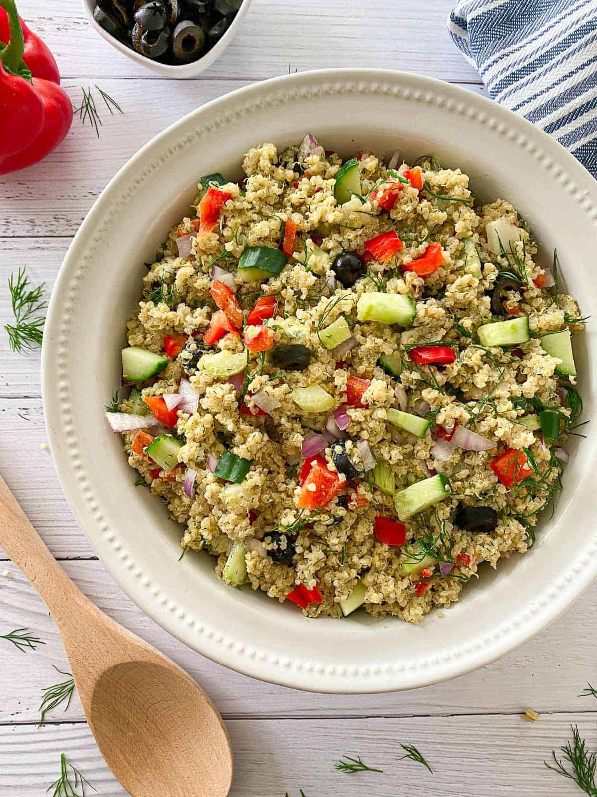 Large bowl of quinoa salad with red pepper, olives, and cucumber.