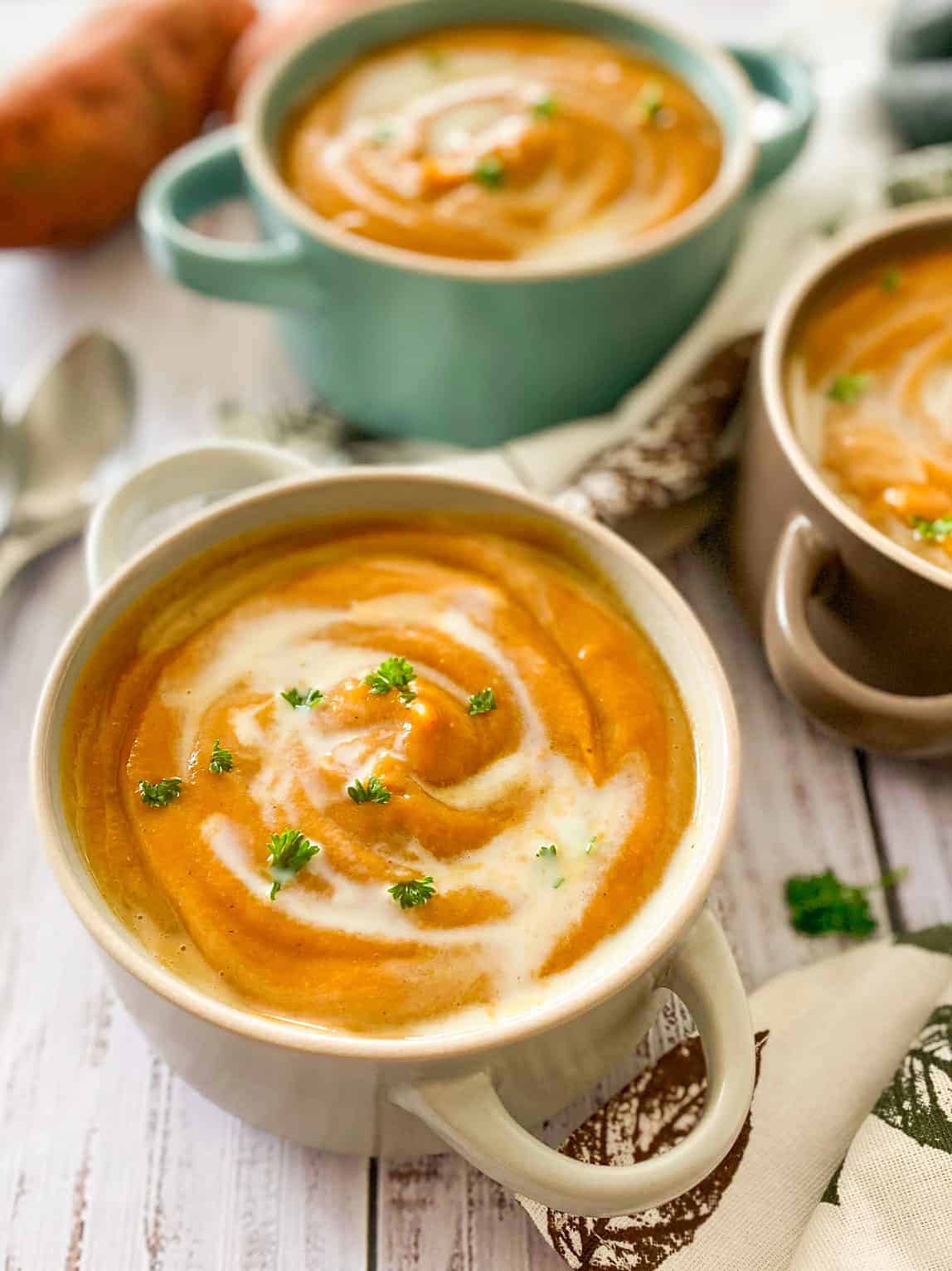 Three bowls of orange creamy soup with parsley garnish.