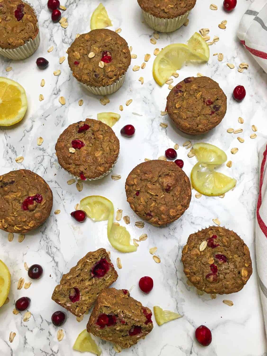 Overhead view of cranberry muffins with cranberries, oats and lemon slices scattered around.