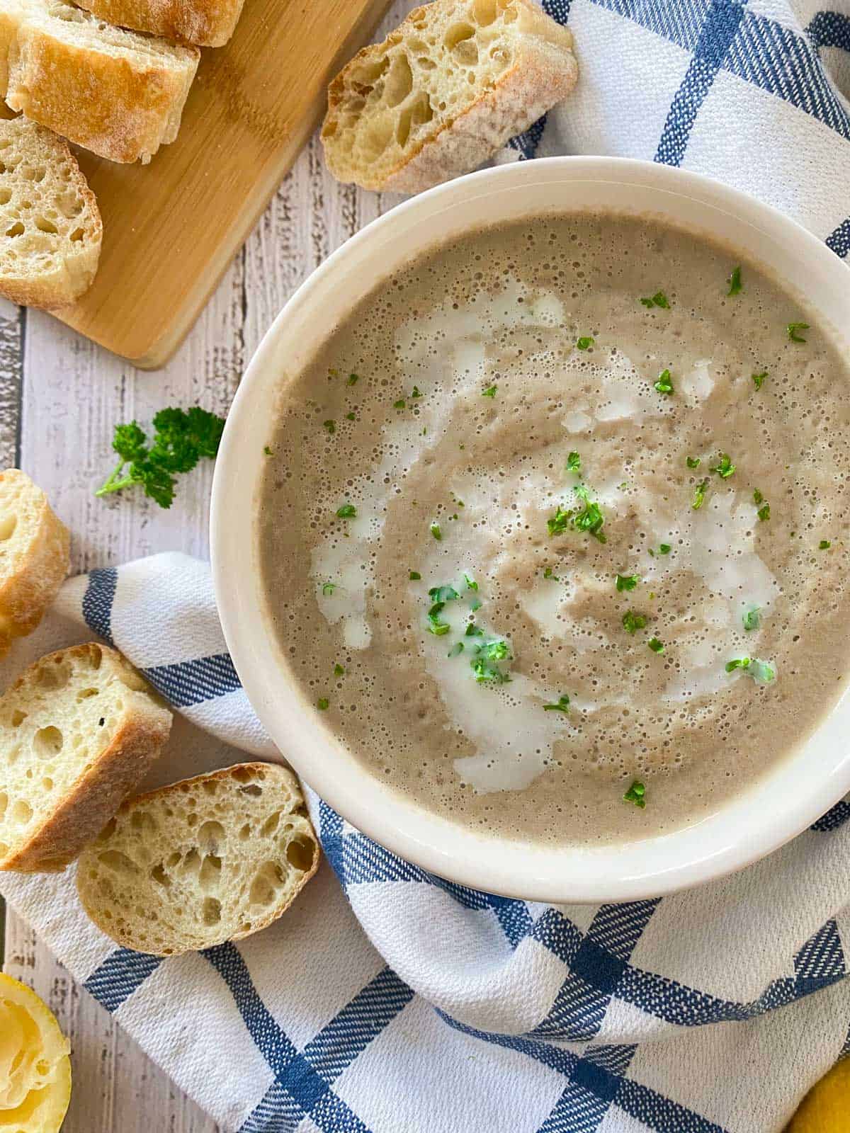Bowl of creamy mushroom soup with baguette slices around the bowl.