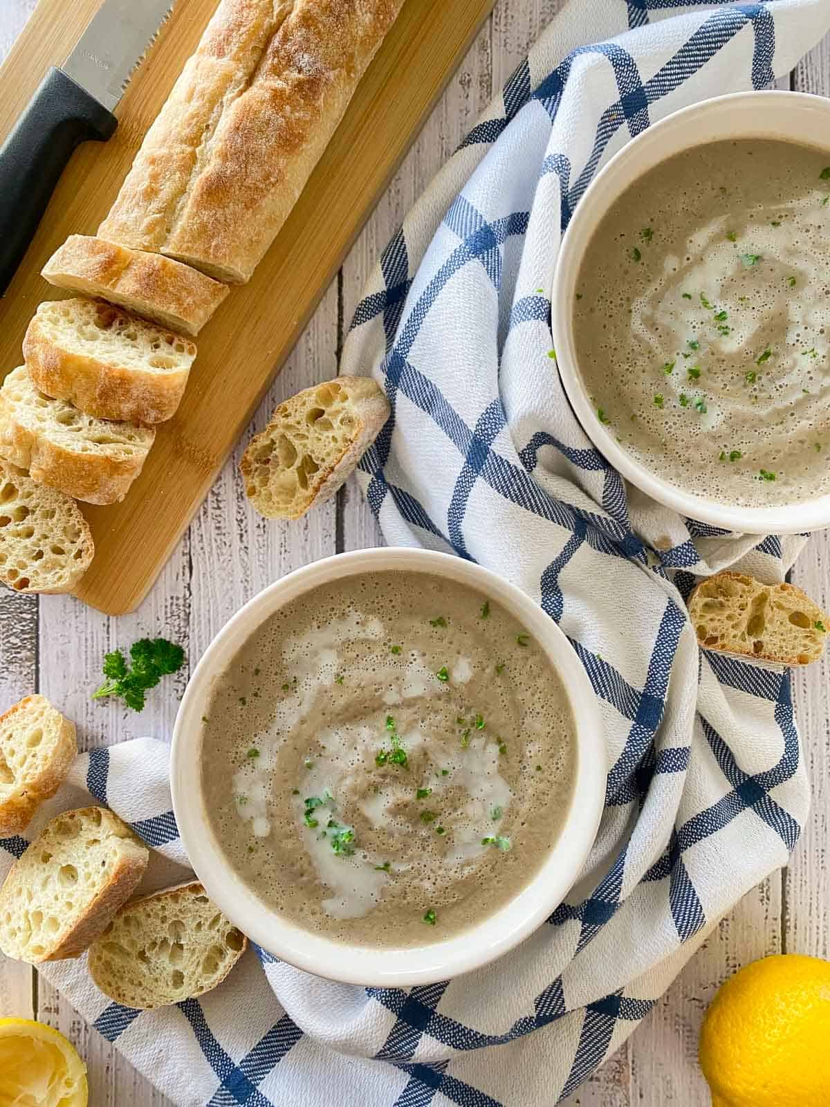 Two bowls filled with mushroom soup and parsley garnish with bread on the side.