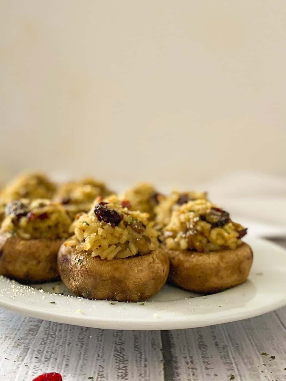 stuffed mushrooms on white platter with cranberries on top.