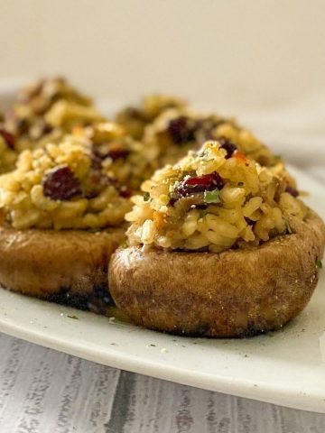 Side view of mushrooms stuffed with risotto and cranberries on white platter.