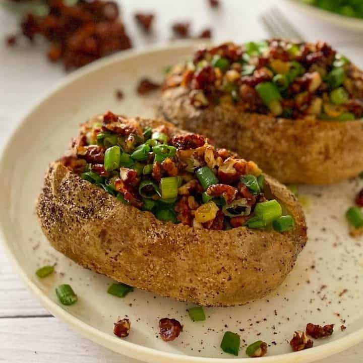 Two baked potatoes in plate, topped with vegan bacon and green onion.