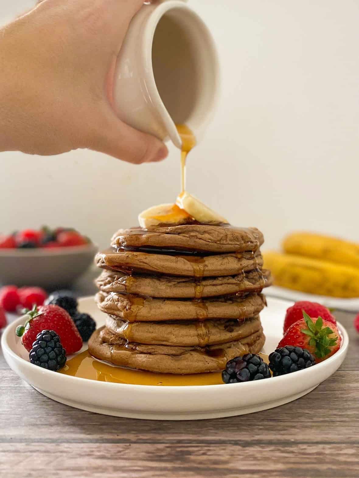 Syrup being poured over stack of pancakes with banana slices on top.
