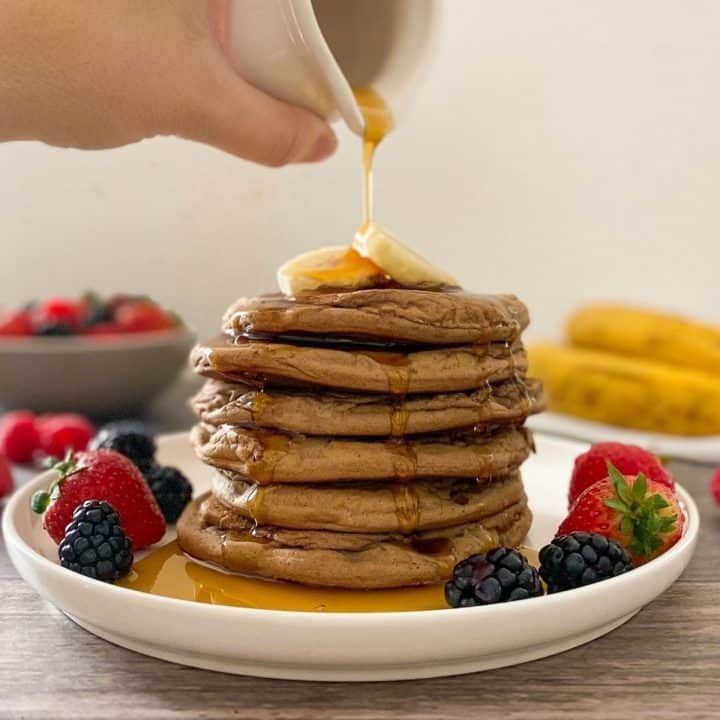 Syrup being poured over stack of pancakes with banana slices on top.