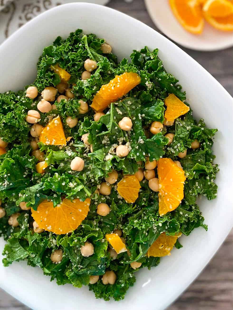 White serving bowl of kale salad with oranges and chickpeas on top.