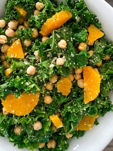 White serving bowl of kale salad with oranges and chickpeas on top.