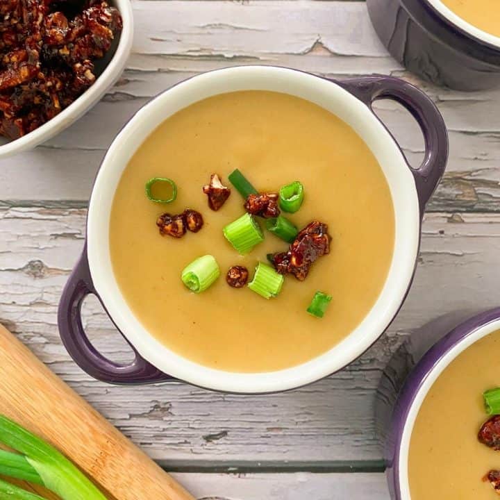 bowl with handles filled potato soup with bacon and chive garnish.