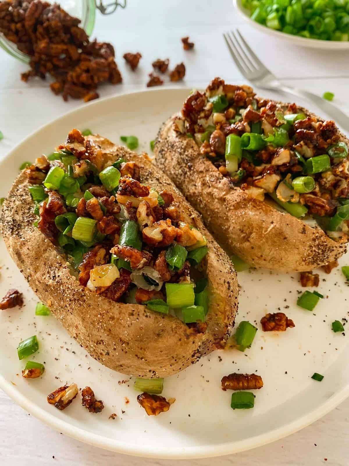 Baked potatoes loaded with bacon and green onion on white plate.