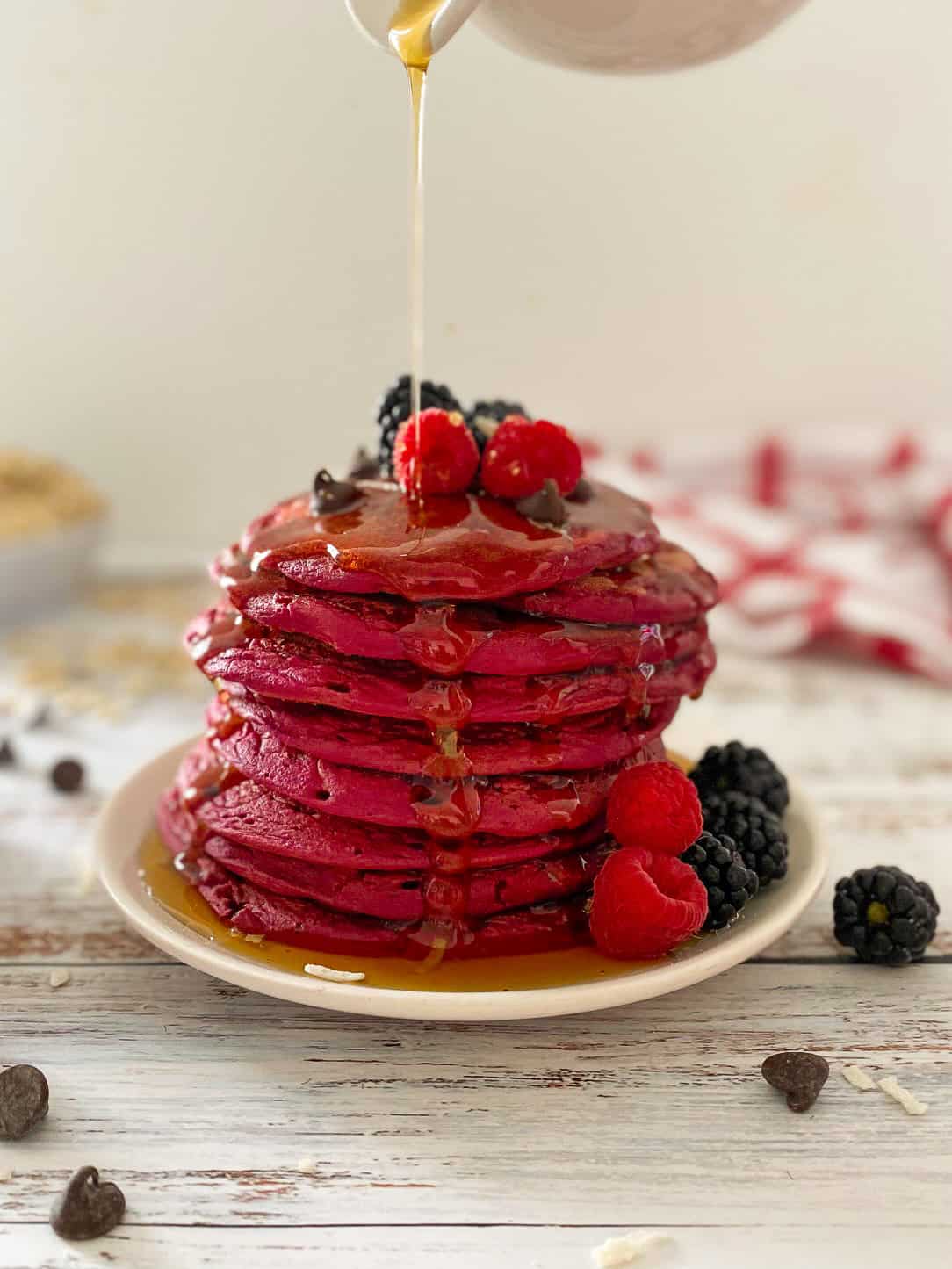 pink pancakes stacked on white plate with syrup dripping down them.
