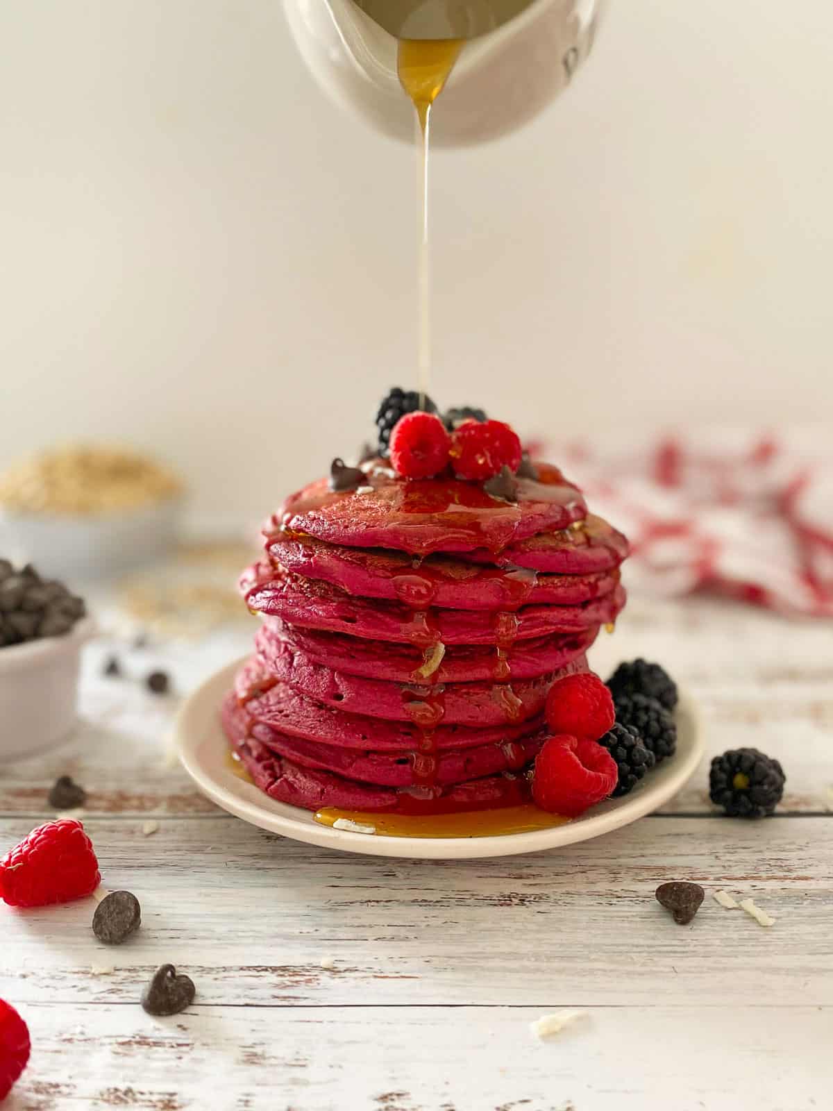 Syrup pouring over stack of pink pancakes with berries on top.