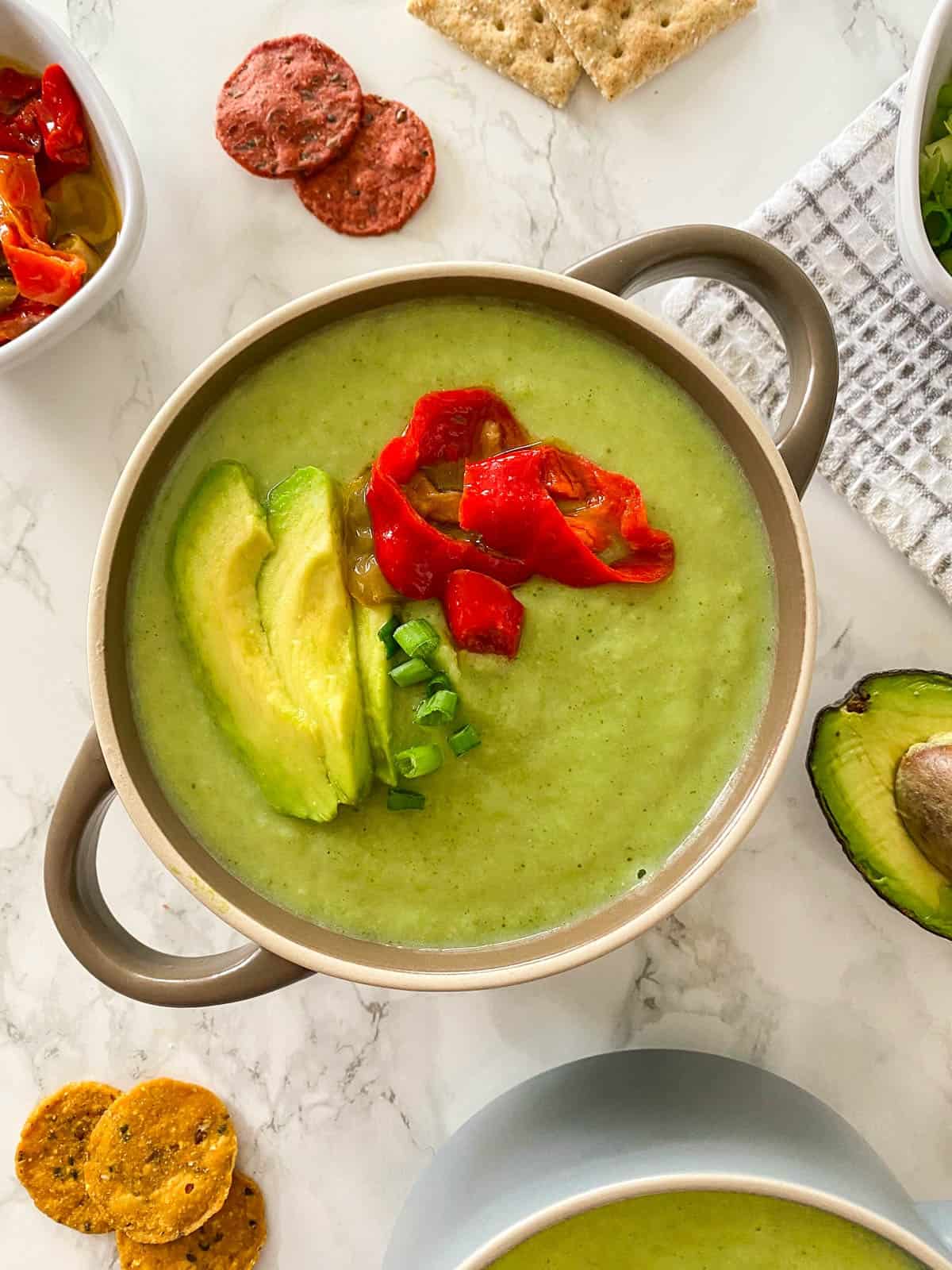 Bowl of broccoli soup with avocado and hot peppers on top.