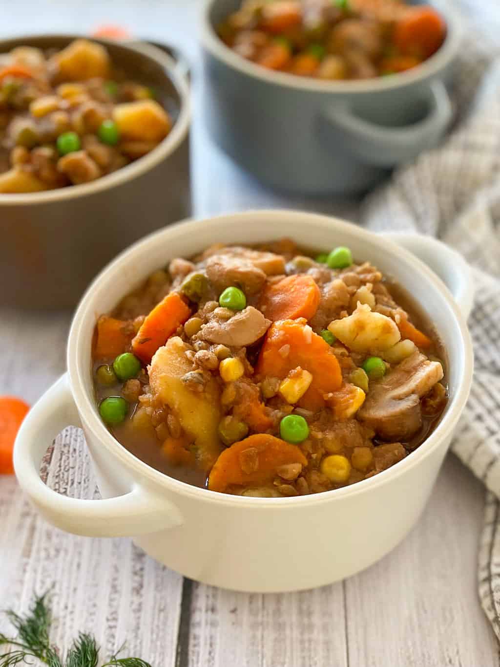 Three bowls filled with vegan stew with carrot, mushrooms, potatoes, peas.