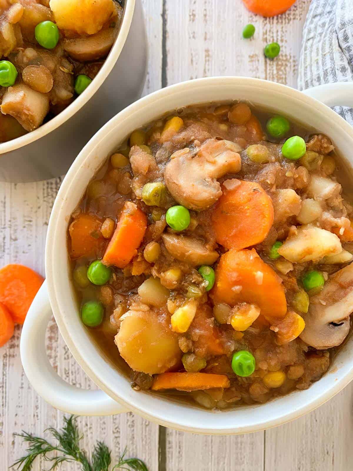 Close up of bowl of stew with mushrooms, carrots, peas, corn, lentils and potatoes.