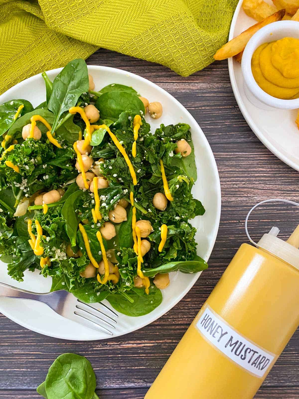 Plate of kale, spinach and chickpea salad with yellow dressing drizzled on top.
