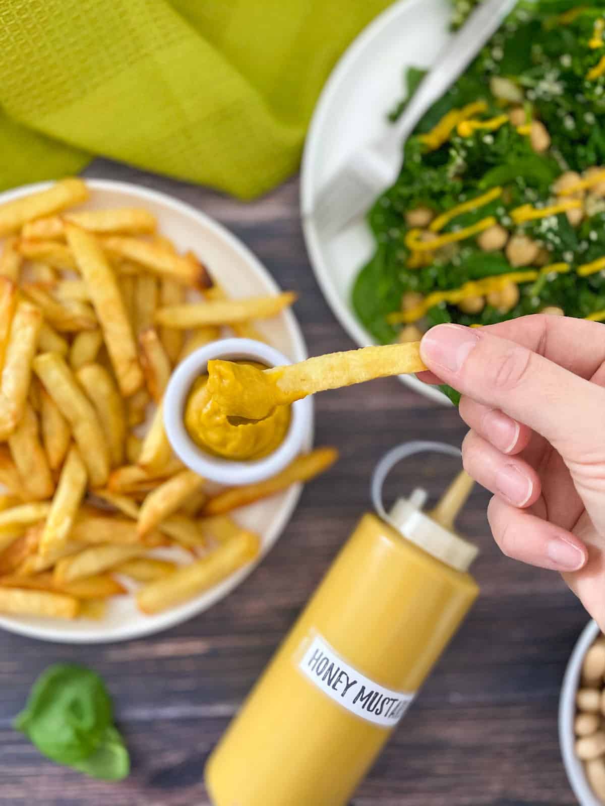 Hand dipping French fry into yellow dip.
