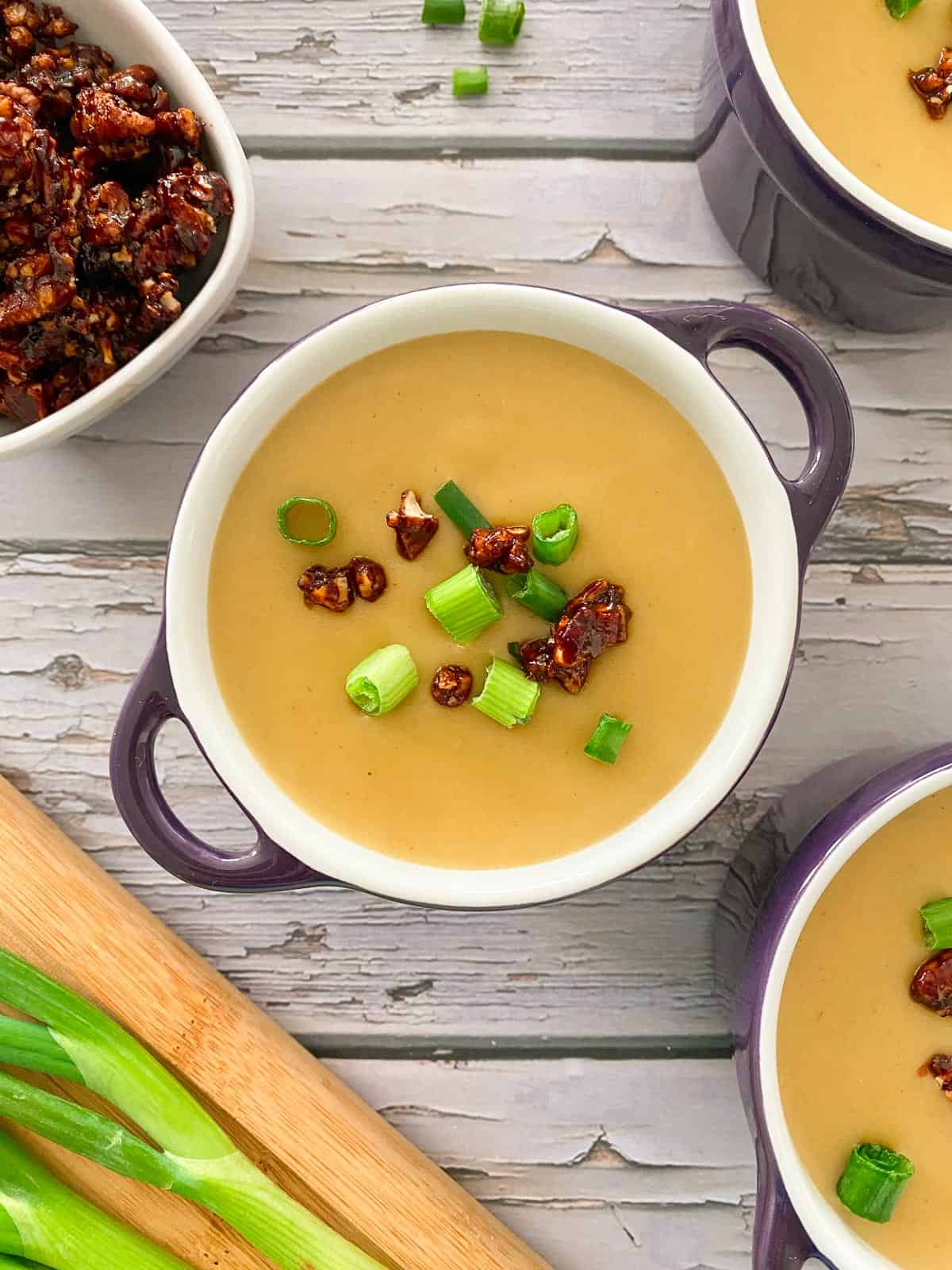 Potato leek soup in purple bowl with handles with pecan bacon and green onion on top.