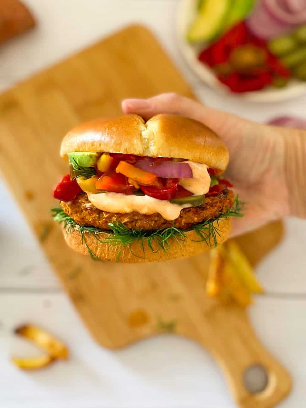 One hand holding up burger with spicy mayo dripping down the side.