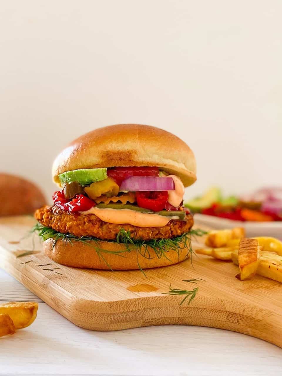 Sweet potato burger in bun with dill, hot peppers, onion and avocado inside.