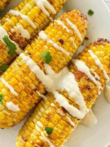 air fryer corn on the cob in platter with crema and cilantro on top.