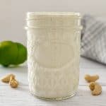 Jar filled with vegan crema fresca with limes in the background.