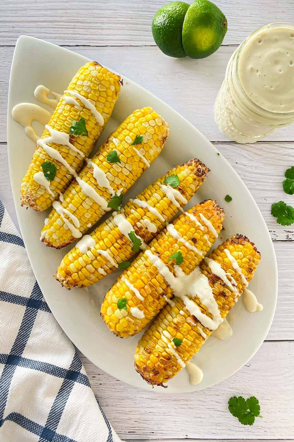 Corn on the cob on white platter with creme fraiche and cilantro garnished on top.