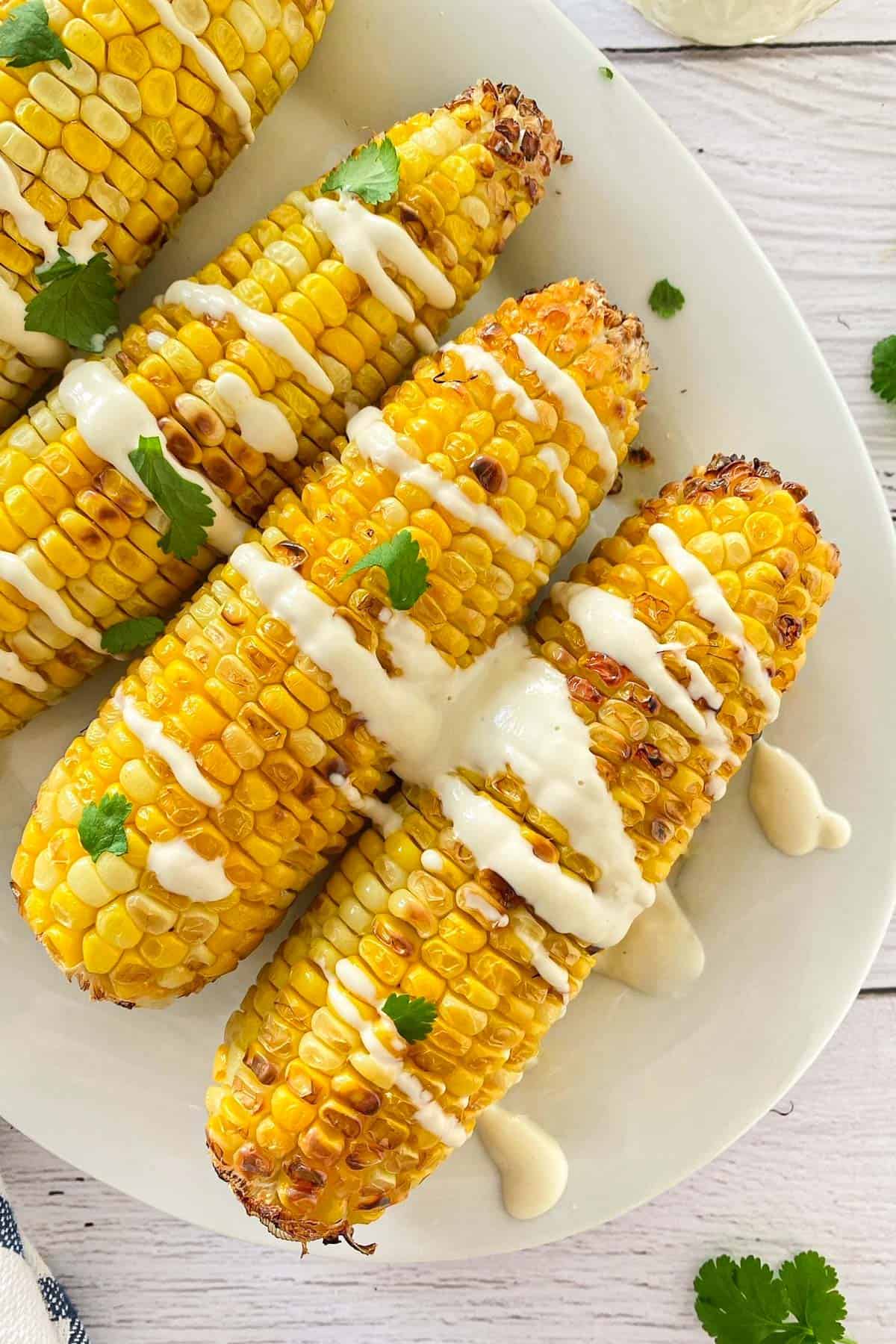 Corn on the cob on platter with crema fresca and cilantro on top.