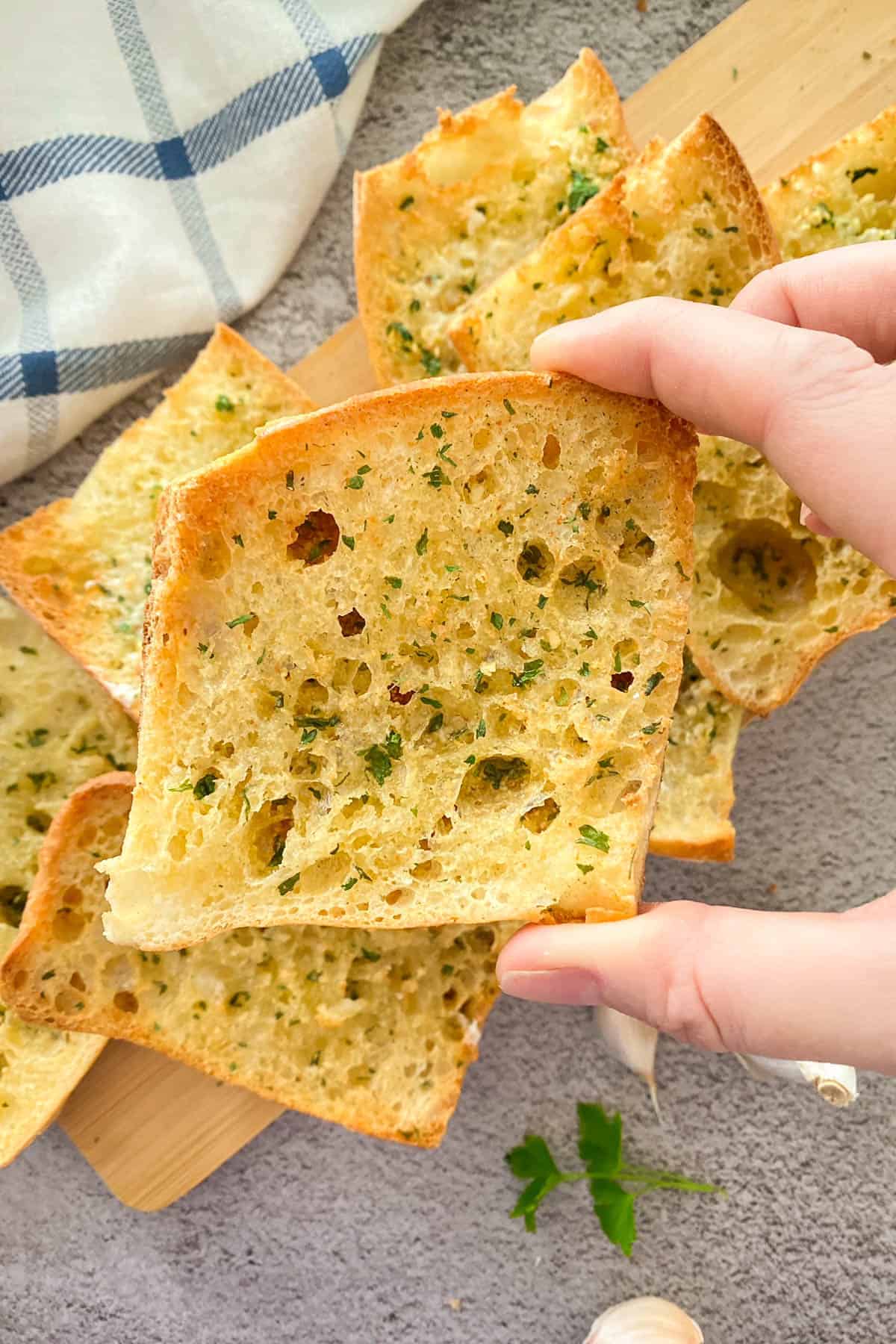Hand holding up slice of garlic bread with more slices below.