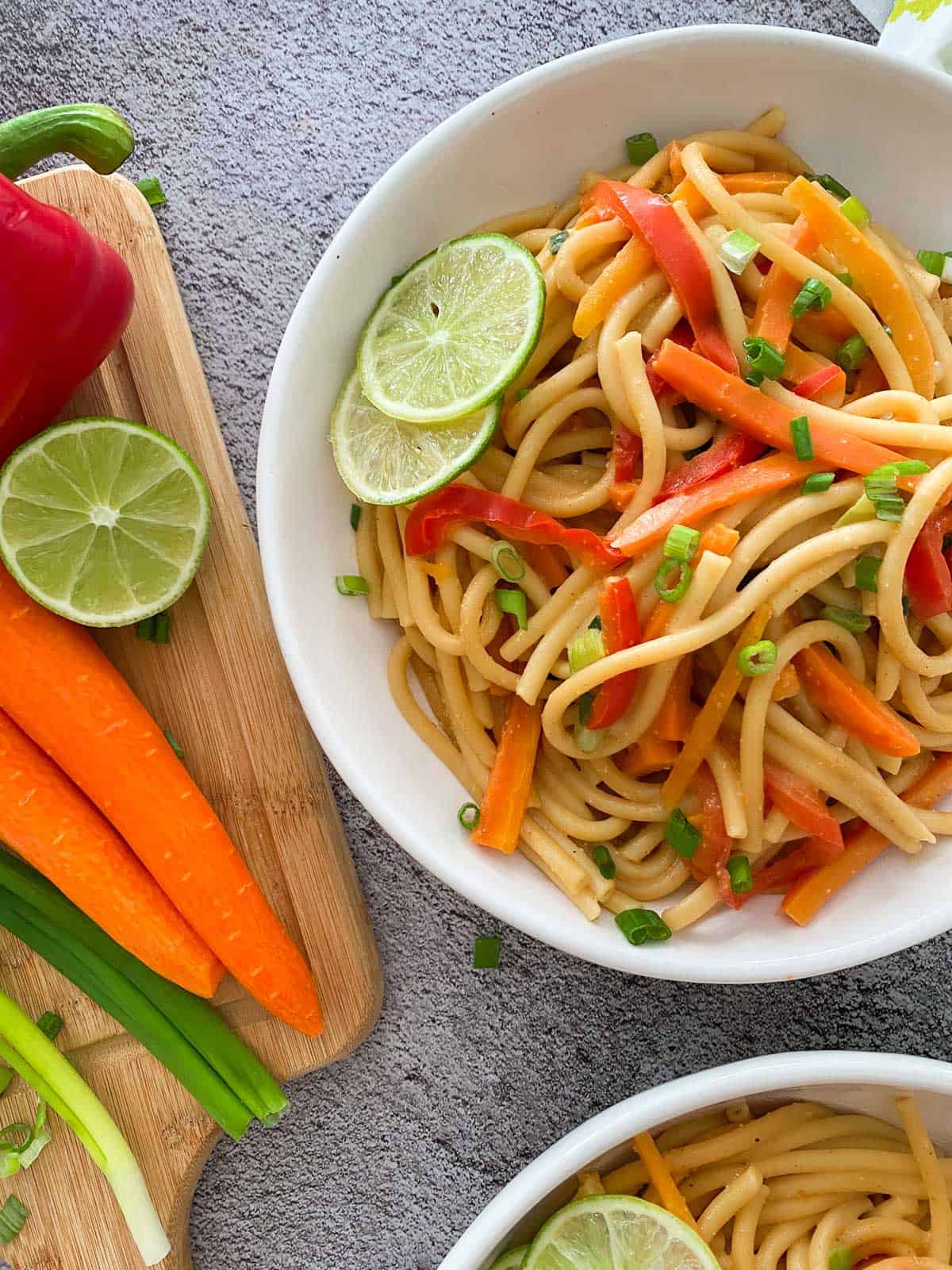 Two plates with peanut noodles with carrots, peppers and lime garnish.