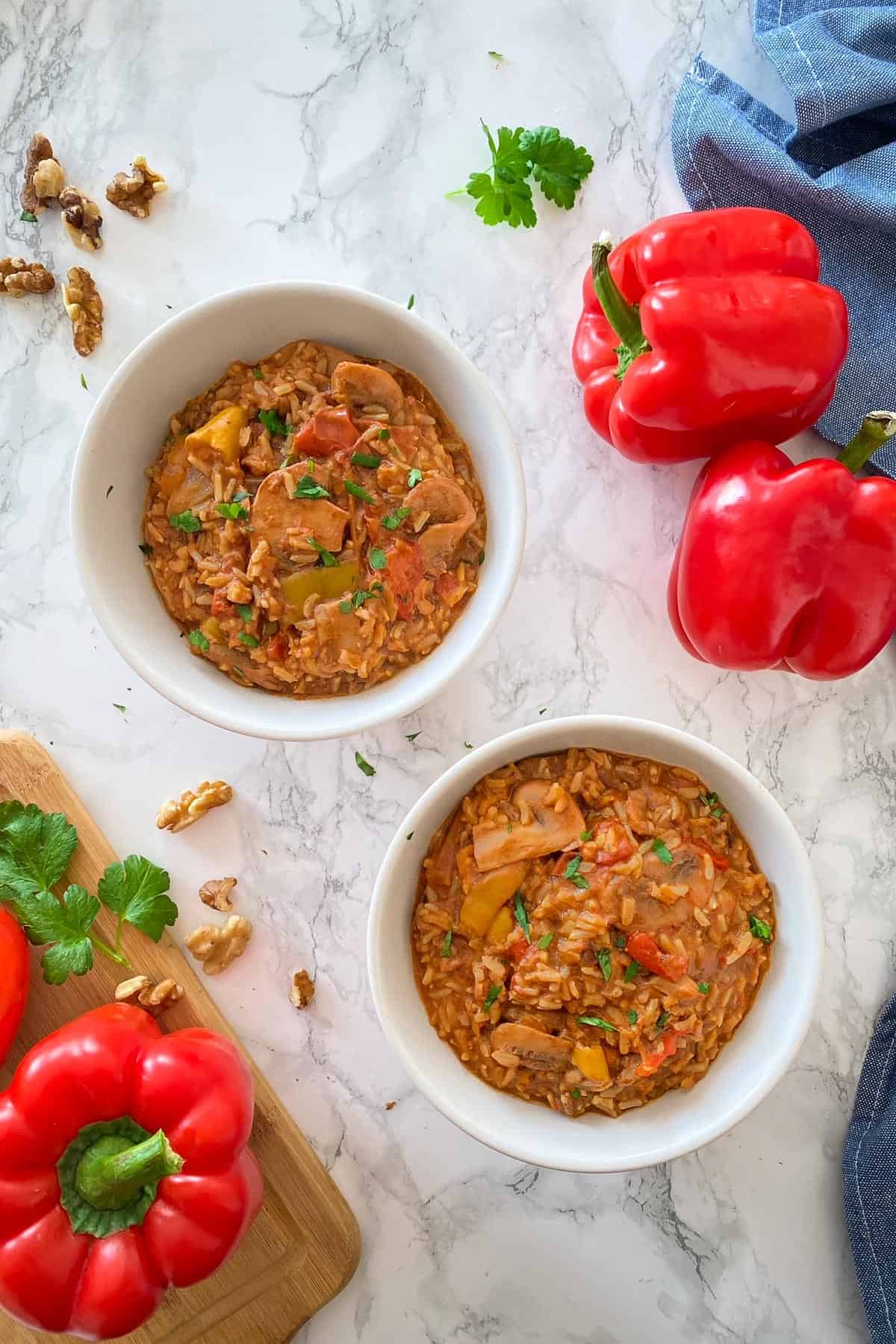 Two bowls filled with rice, mushrooms, peppers in a tomato base sauce with parsley garnish.
