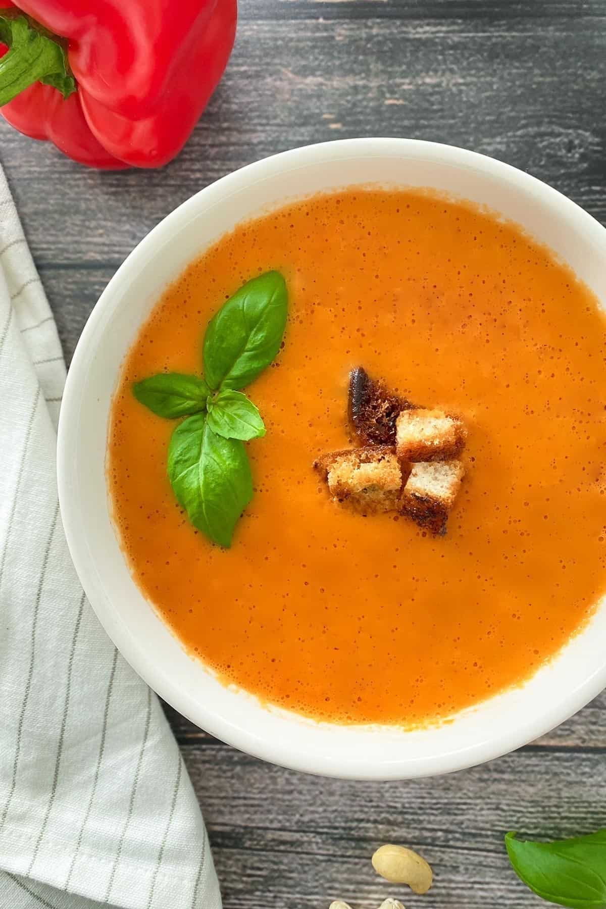 White bowl full of tomato soup with basil and croutons on top.