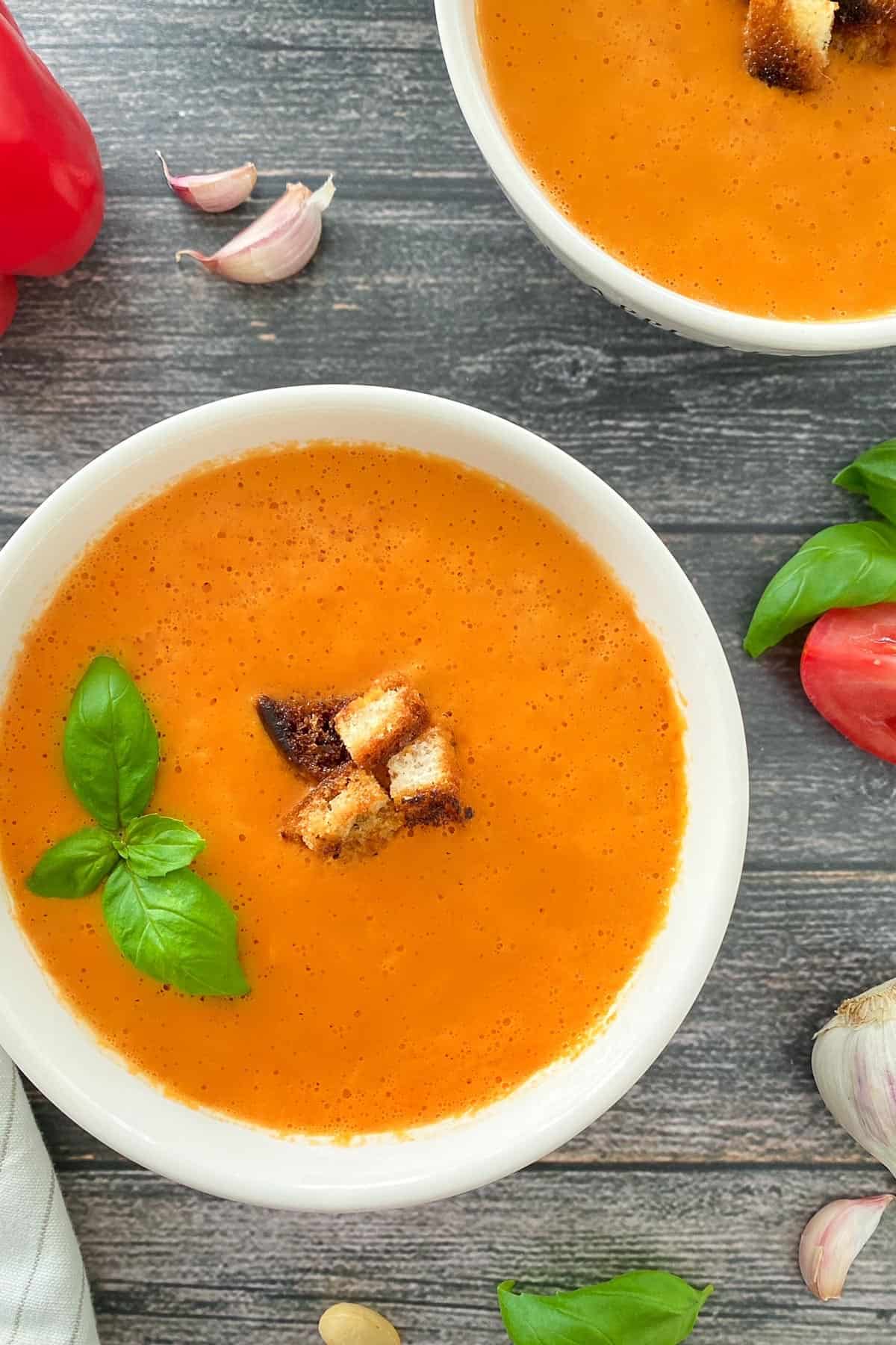 Two bowls of tomato soup with croutons in the center and basil garnish.